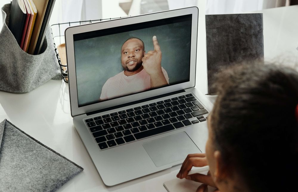 foto de uma mulher assistindo a um vídeo em um notebook disposto sobre uma mesa