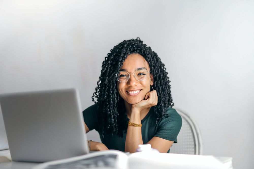 foto de uma mulher negra, de cabelos cacheados na altura do ombro, ela está sentada, olhando para a frente e sorrindo