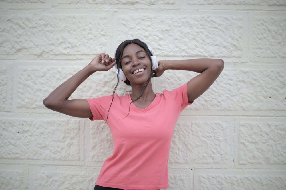 mulher negra de camiseta rosa com fones de ouvido em frente a uma parede branca