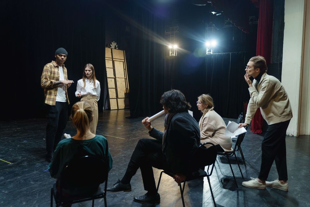 Grupo de teatro com seis integrantes reunido em um palco em momento de ensaio