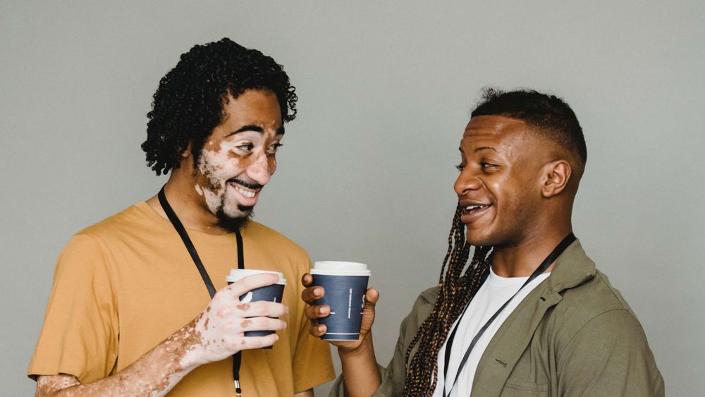 Dois homens negros se olhando com copos de café na mão. Eles sorriem.