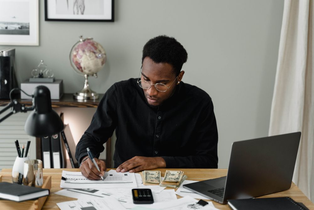 homem negro de cabelo curto sentado em uma mesa de trabalho com computador