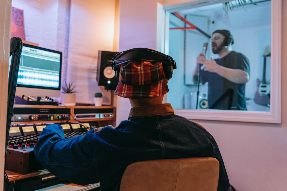 homem em estúdio de gravação de música observando outro homem dentro de um aquário de gravação de voz
