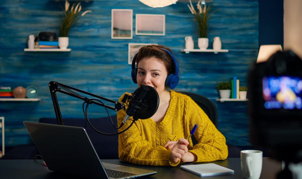 Uma mulher usando fones de ouvidos azul, falando no microfone. 